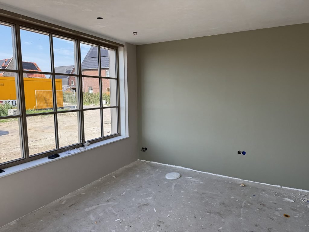 Nieuwbouwkamer met een groot roedenraam en een geverfde wand in zachtgroen, kort na het behangen