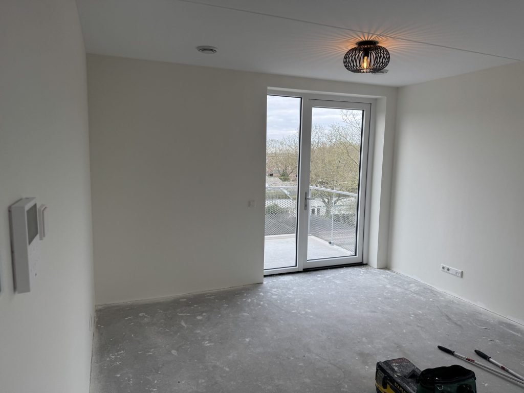 Lichte lege kamer met balkondeuren en een hanglamp, de muren net wit afgewerkt